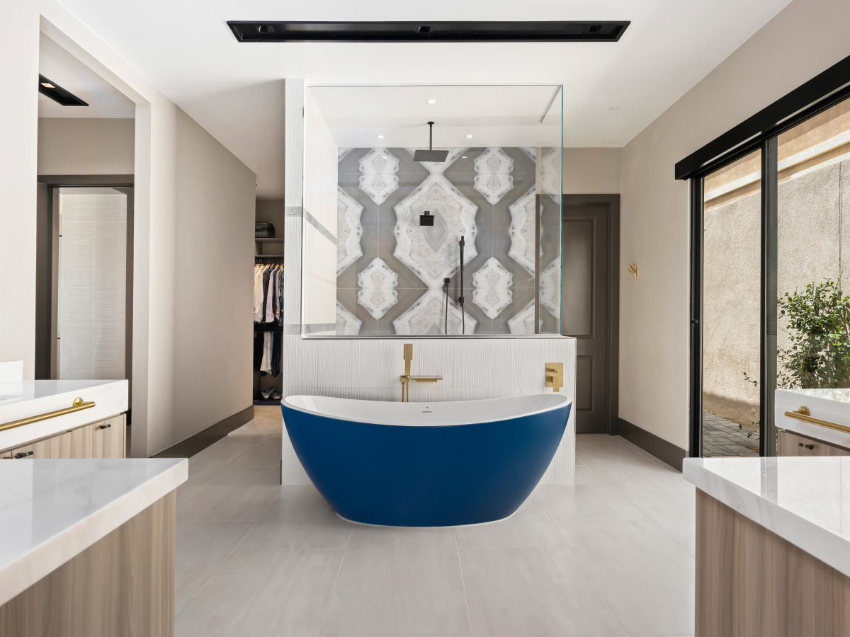 Primary bathroom with cobalt blue freestanding tub, striking porcelain slab shower wall, and gold fixtures, Reveal Interior Design Las Vegas