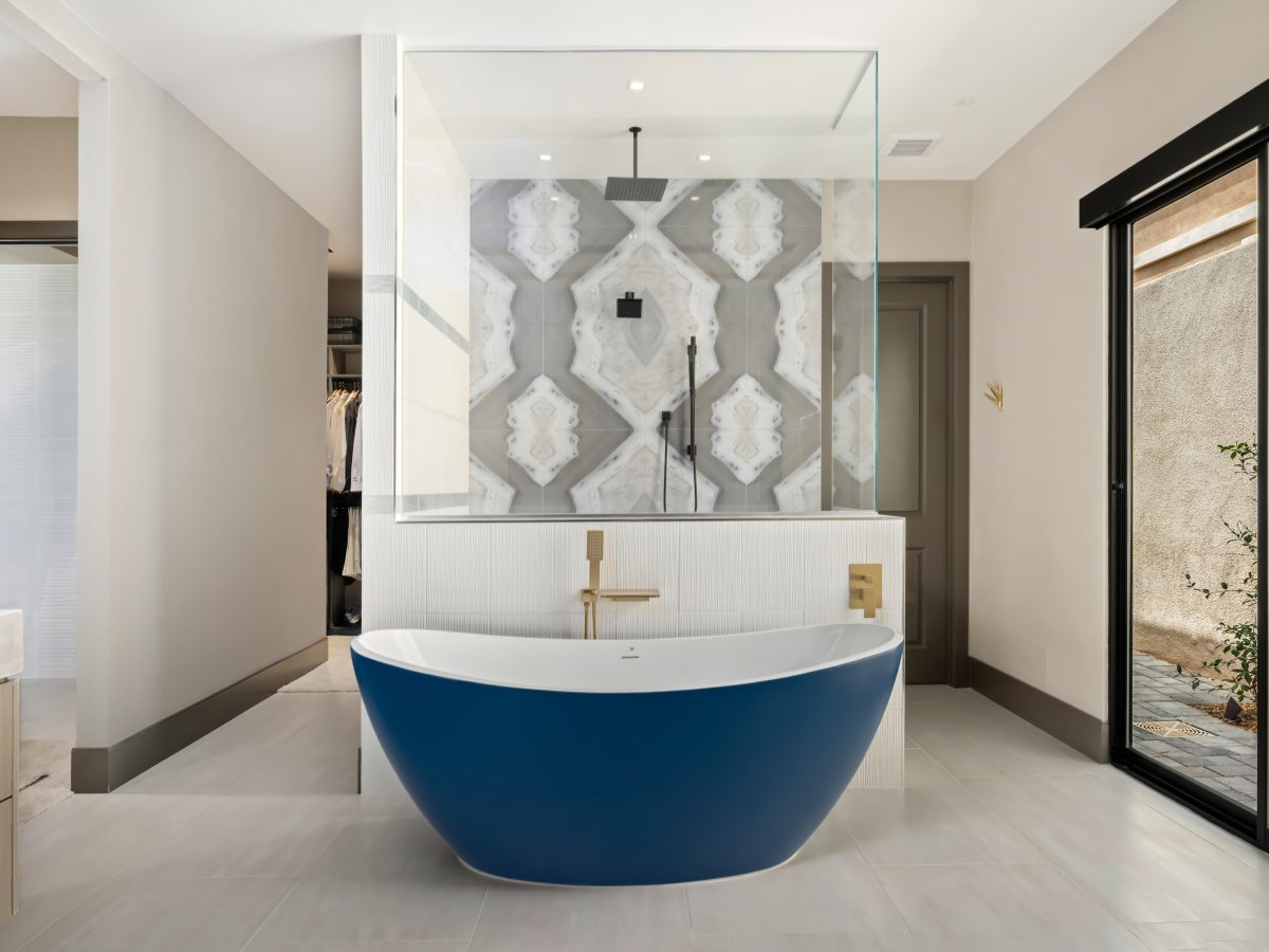 Primary bathroom with cobalt blue freestanding tub, porcelain slab shower wall, and gold fixtures, Reveal Interior Design Las Vegas