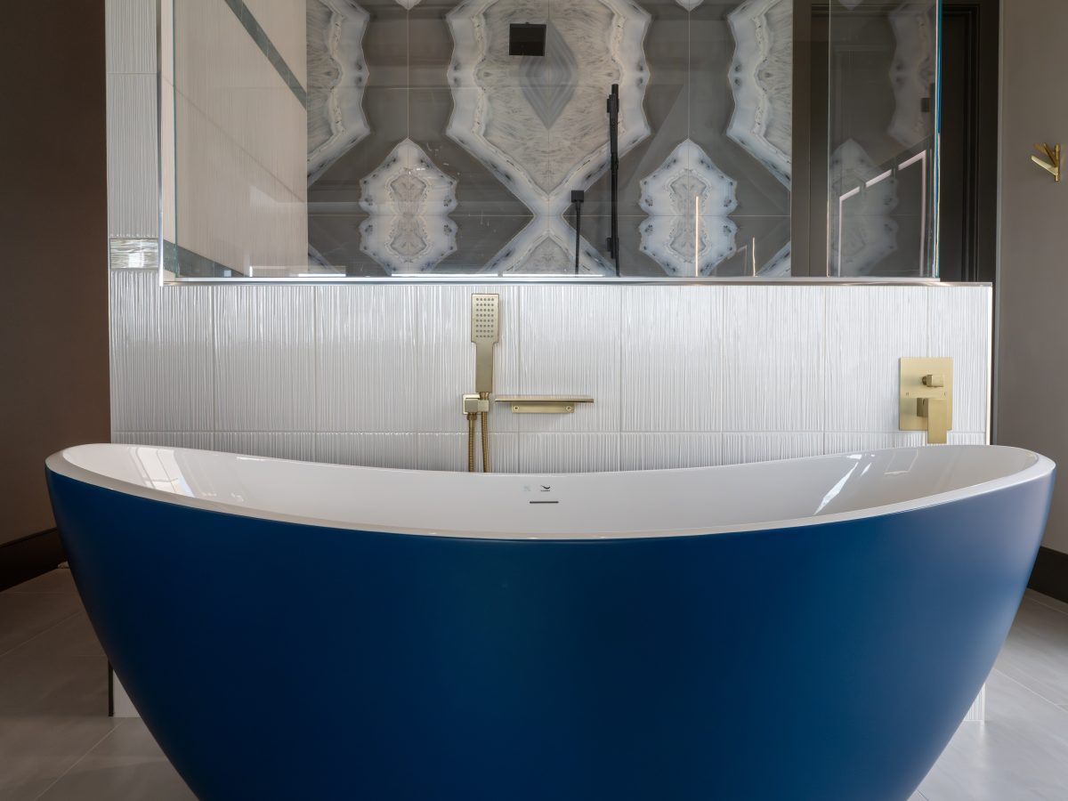 Primary bathroom with cobalt blue freestanding tub, gold fixtures, and porcelain slab shower wall, Reveal Interior Design Las Vegas