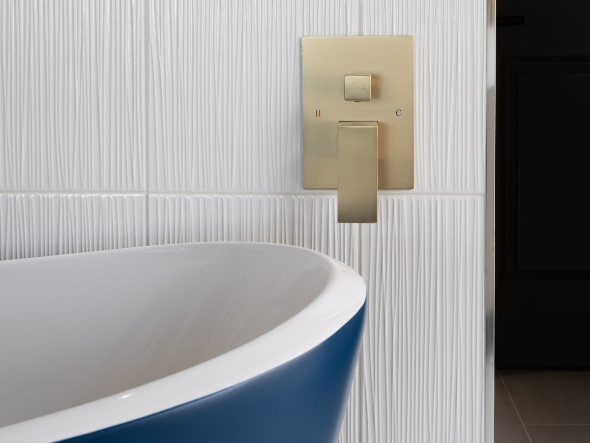 Primary bathroom with cobalt blue freestanding tub, textured white porcelain tile wall, and brushed gold fixtures, Reveal Interior Design Las Vegas