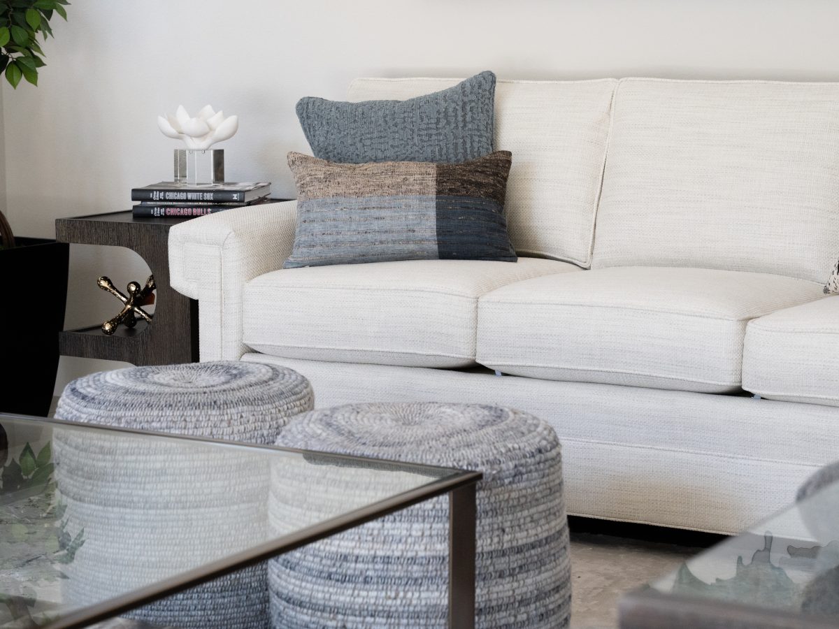 Living room with custom off-white sofa, natural threaded poufs, and layered blue-gray pillows, Reveal Interior Design Las Vegas
