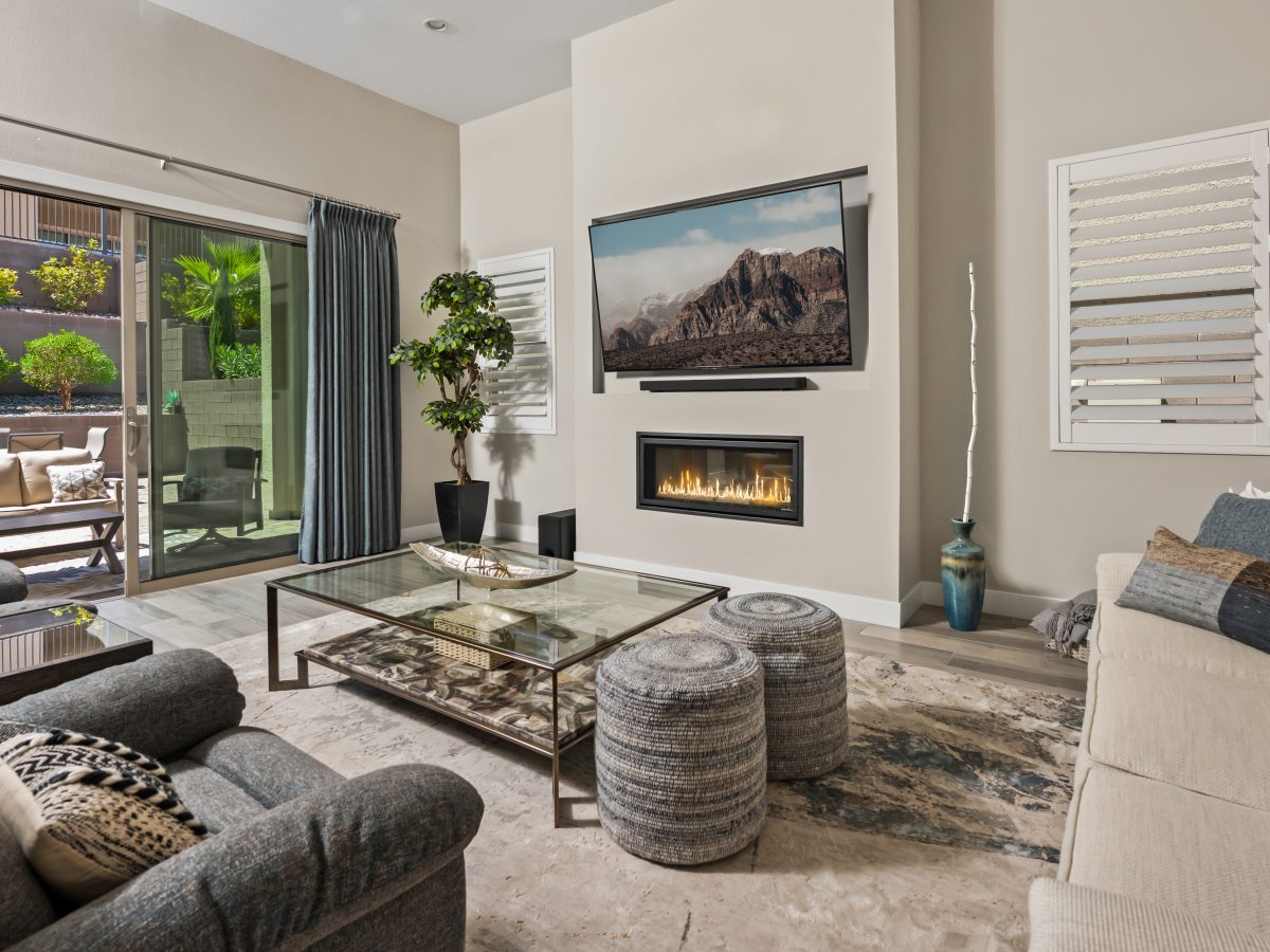 Contemporary living room with stone-and-bronze coffee table, gas fireplace, and wall-mounted TV, Reveal Interior Design Las Vegas