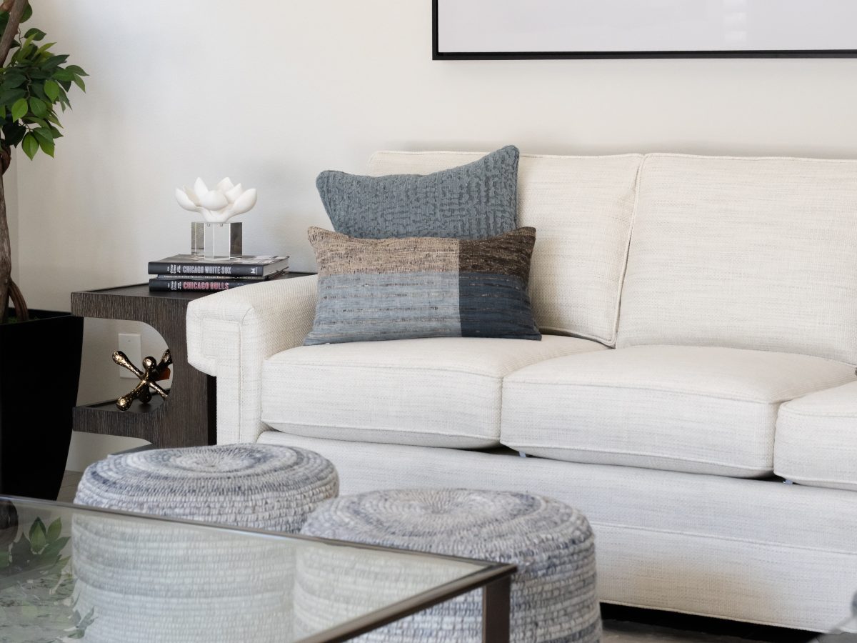 Contemporary living room with custom off-white sofa, natural threaded poufs, and stone-and-bronze coffee table, Reveal Interior Design Las Vegas