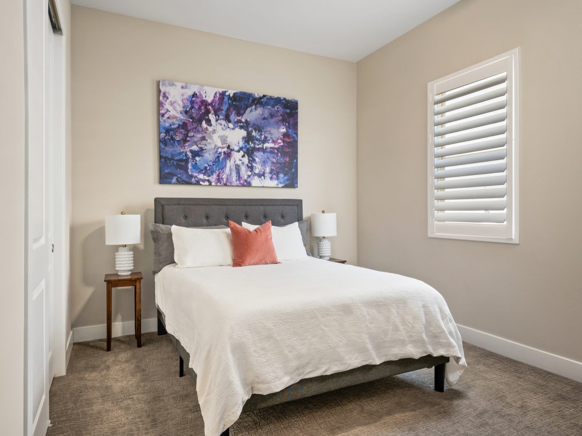 Guest bedroom with tufted upholstered bed frame, abstract expressionist artwork, and plantation shutters, Reveal Interior Design Las Vegas