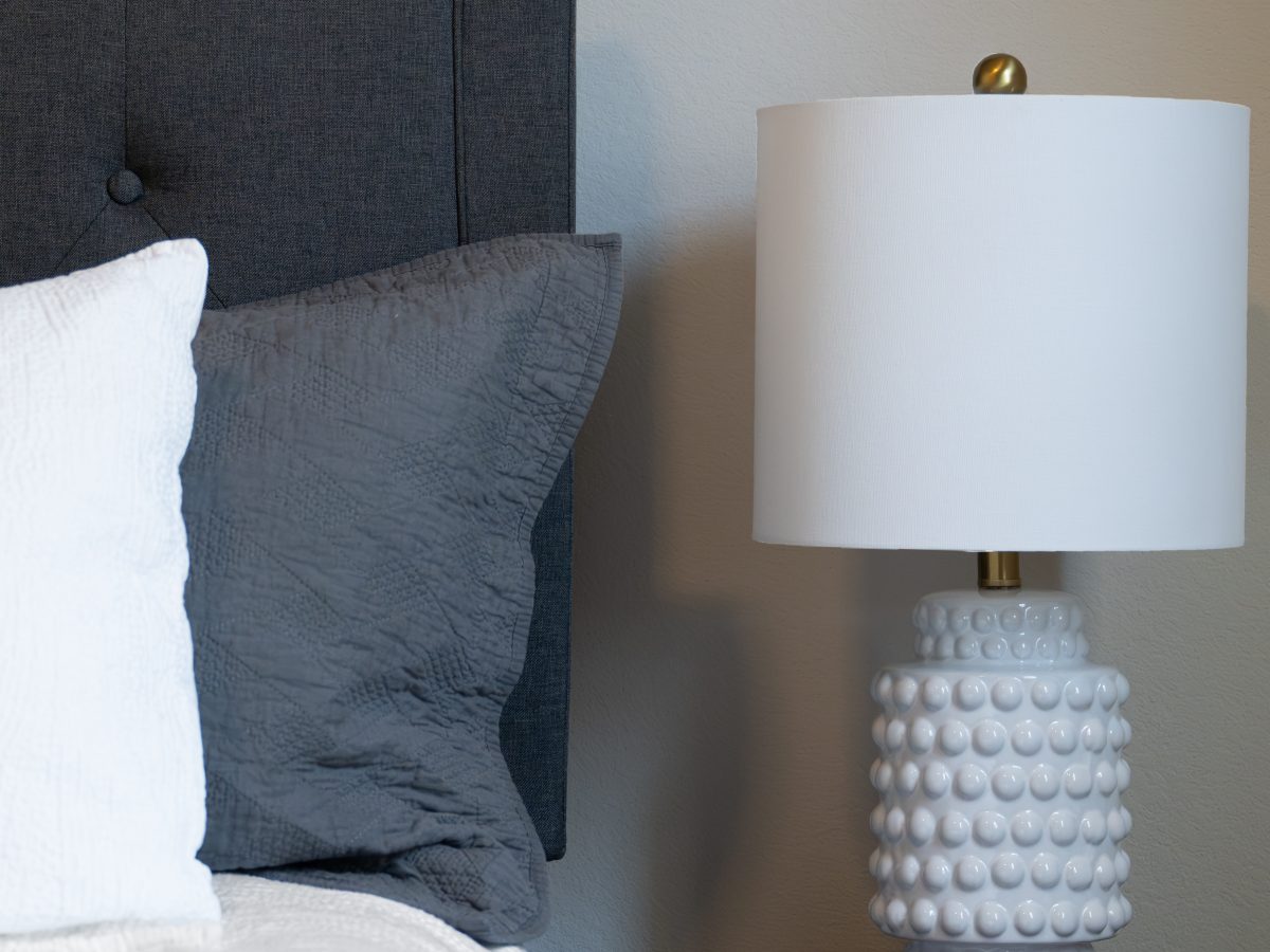 Contemporary bedroom vignette with charcoal upholstered headboard and hobnail ceramic table lamp, Reveal Interior Design Las Vegas