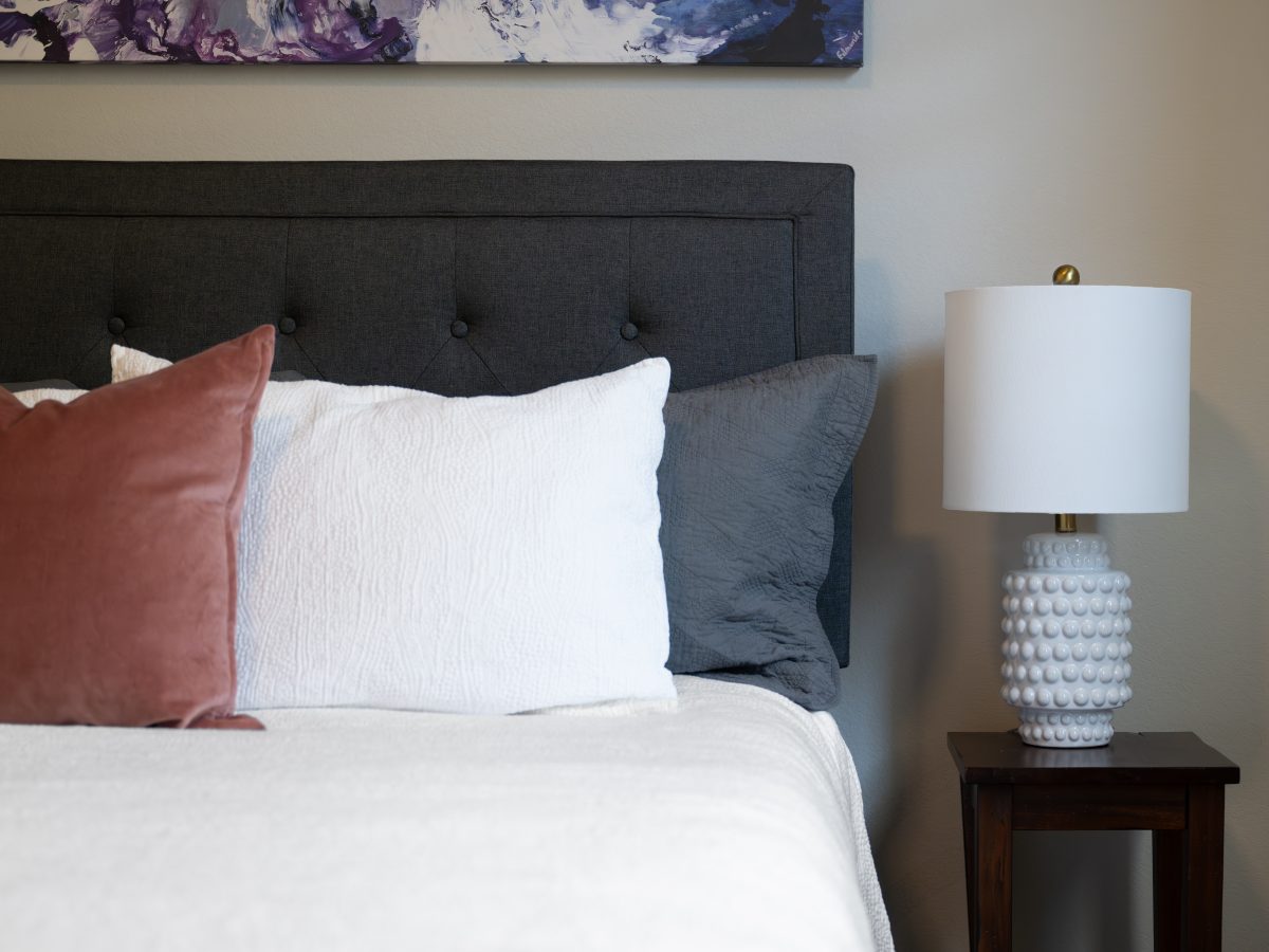 Primary bedroom with tufted charcoal upholstered headboard and layered pillow styling, Reveal Interior Design Las Vegas