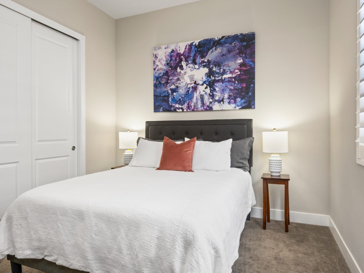 Guest bedroom with tufted charcoal headboard and bold abstract artwork in blues and purples, Reveal Interior Design Las Vegas