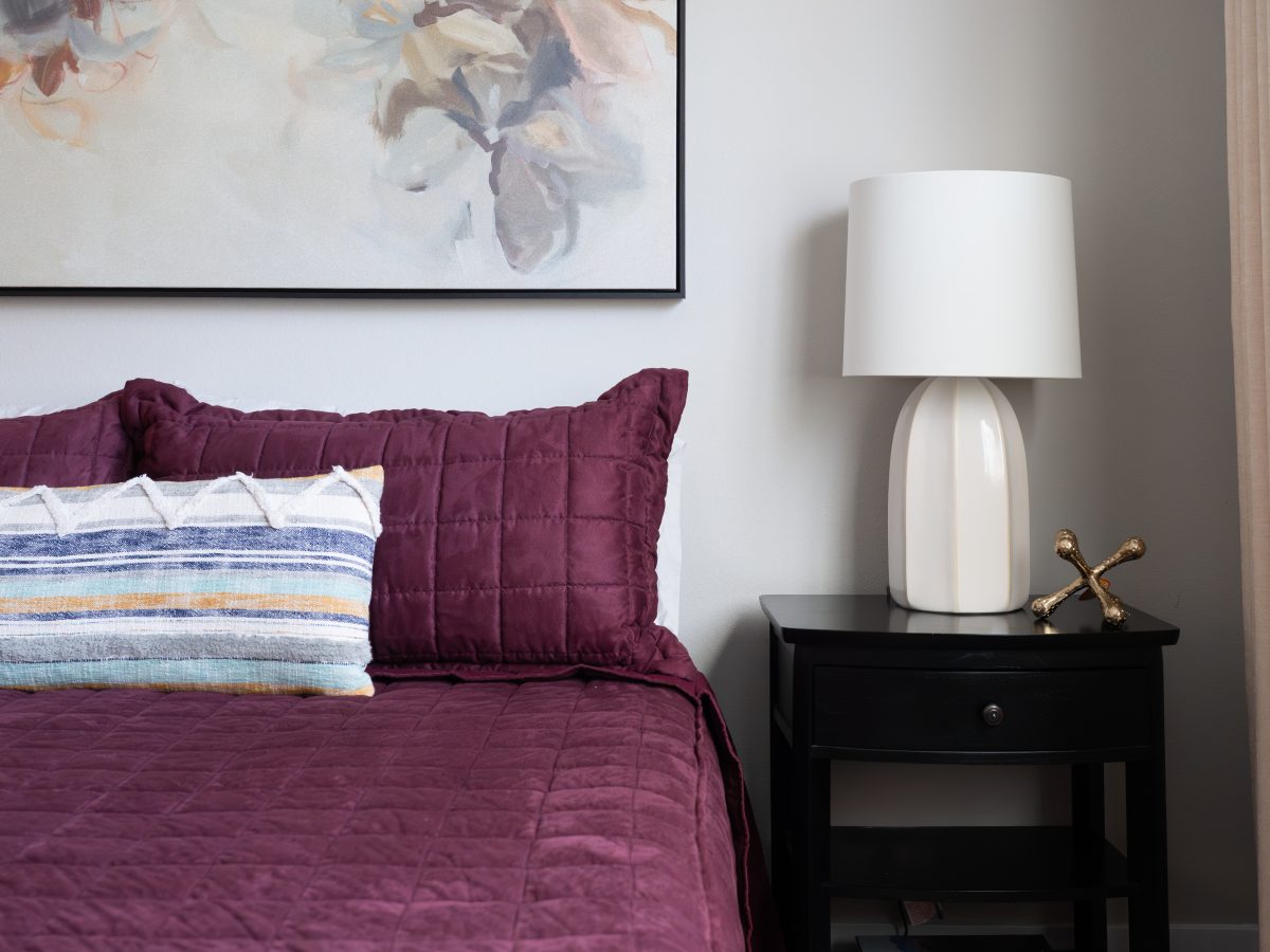 Bedroom with deep plum quilted bedding, floral botanical artwork, and black nightstand, Reveal Interior Design Las Vegas