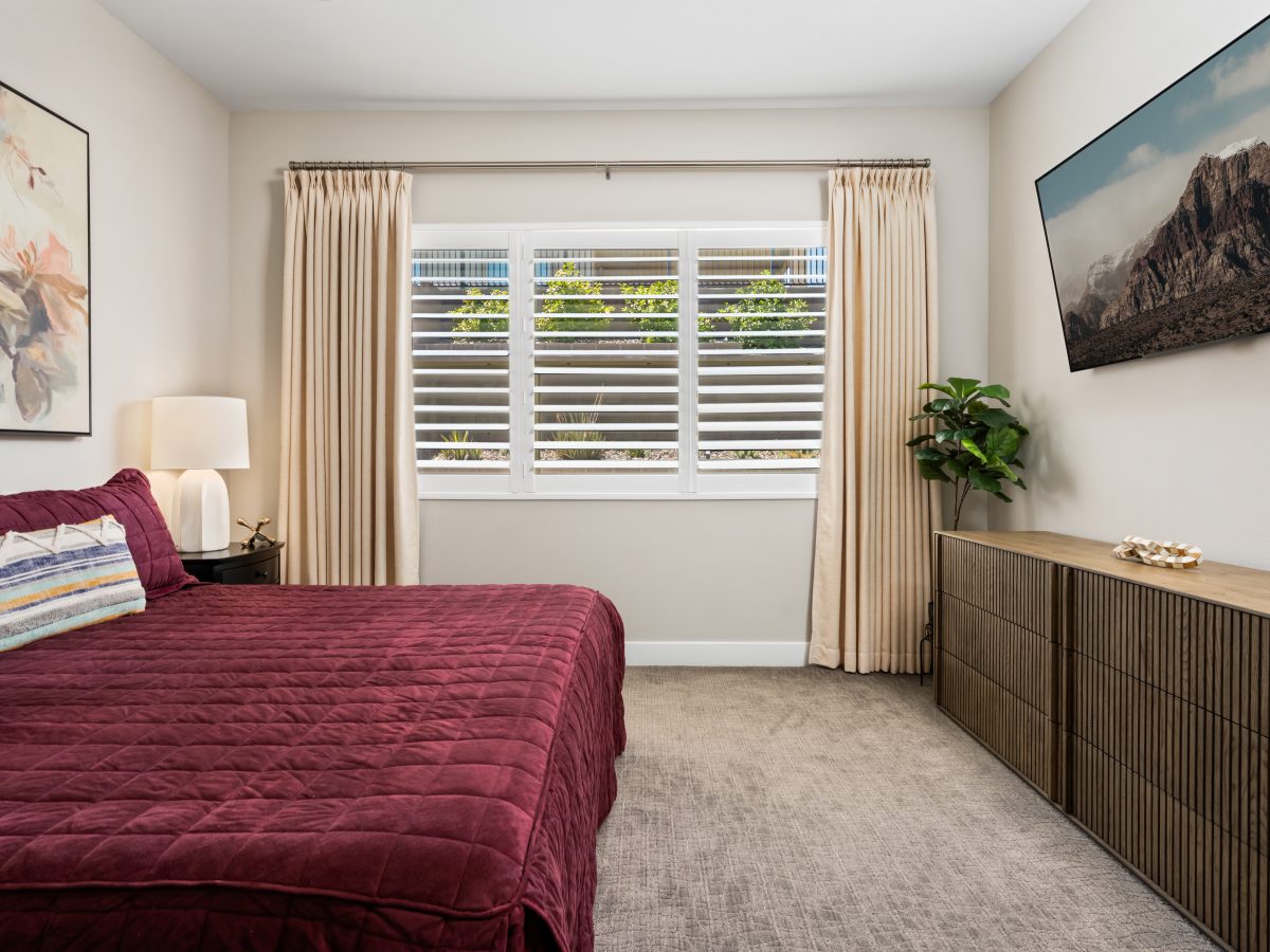 Primary bedroom with cranberry velvet bedding, sand draperies, and plantation shutters, Reveal Interior Design Las Vegas