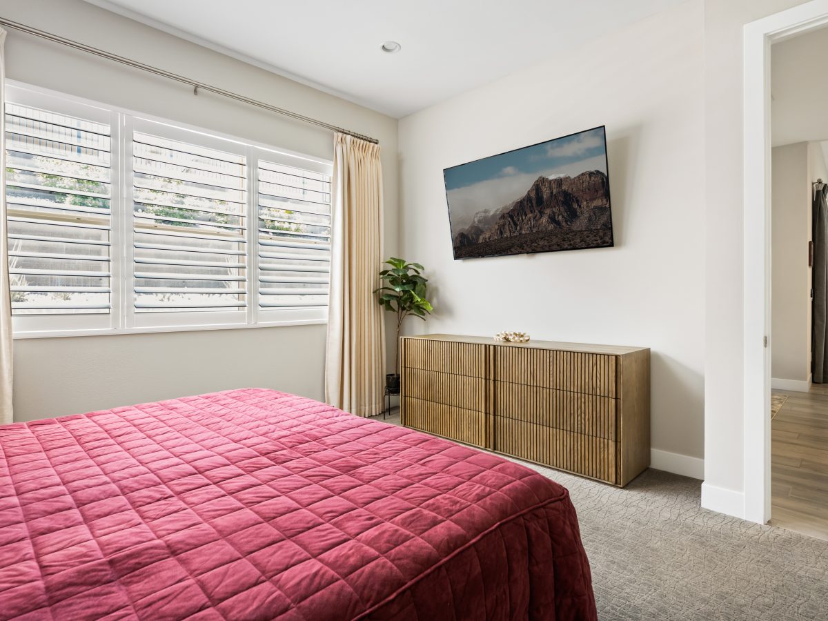 Primary bedroom with cranberry velvet comforter, textured light-brown dresser, and sand draperies, Reveal Interior Design Las Vegas