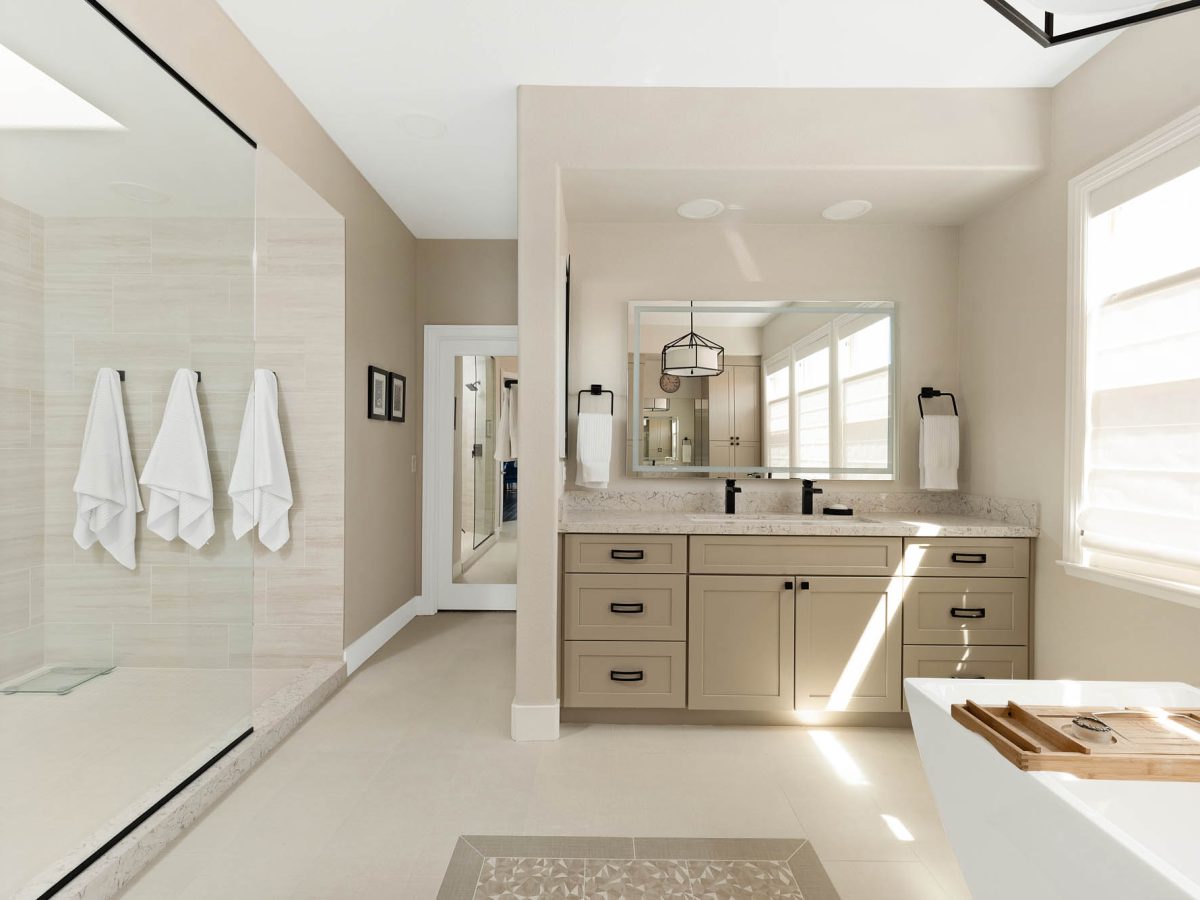 Primary bathroom with warm beige cabinetry, quartz countertops, and freestanding tub, Reveal Interior Design Las Vegas
