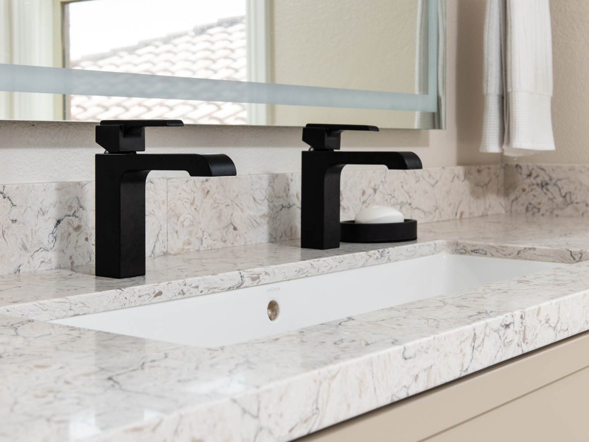 Primary bathroom trough sink with white and beige veined quartz countertop and dual black single-hole faucets, Reveal Interior Design Las Vegas