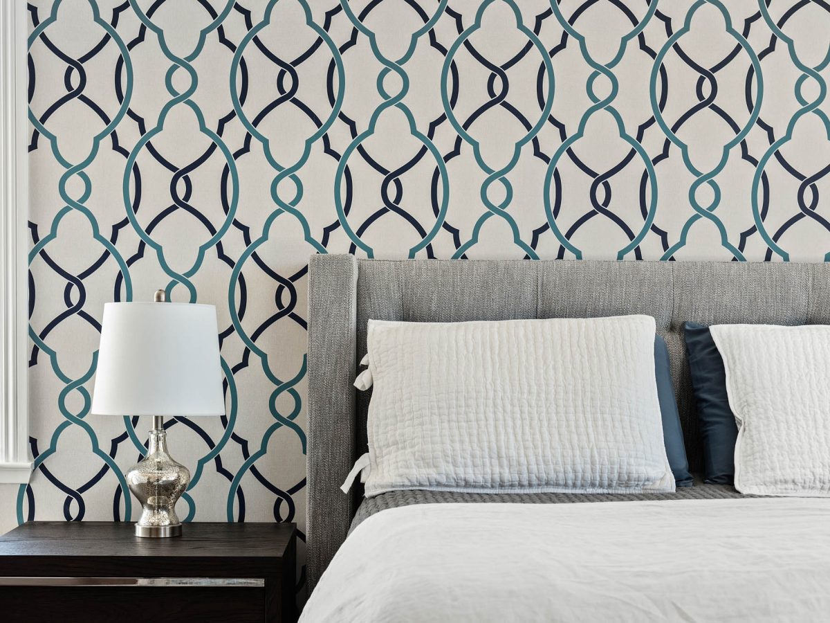 Primary bedroom with teal and navy geometric wallpaper accent wall and gray upholstered king bed, Reveal Interior Design Las Vegas