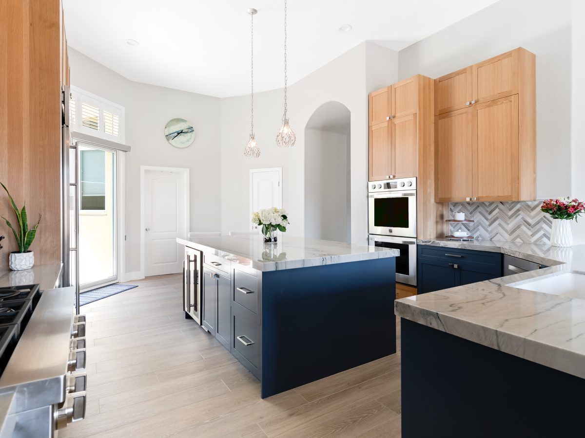 Kitchen with navy blue base cabinets, warm oak uppers, and quartzite countertops, Reveal Interior Design Las Vegas