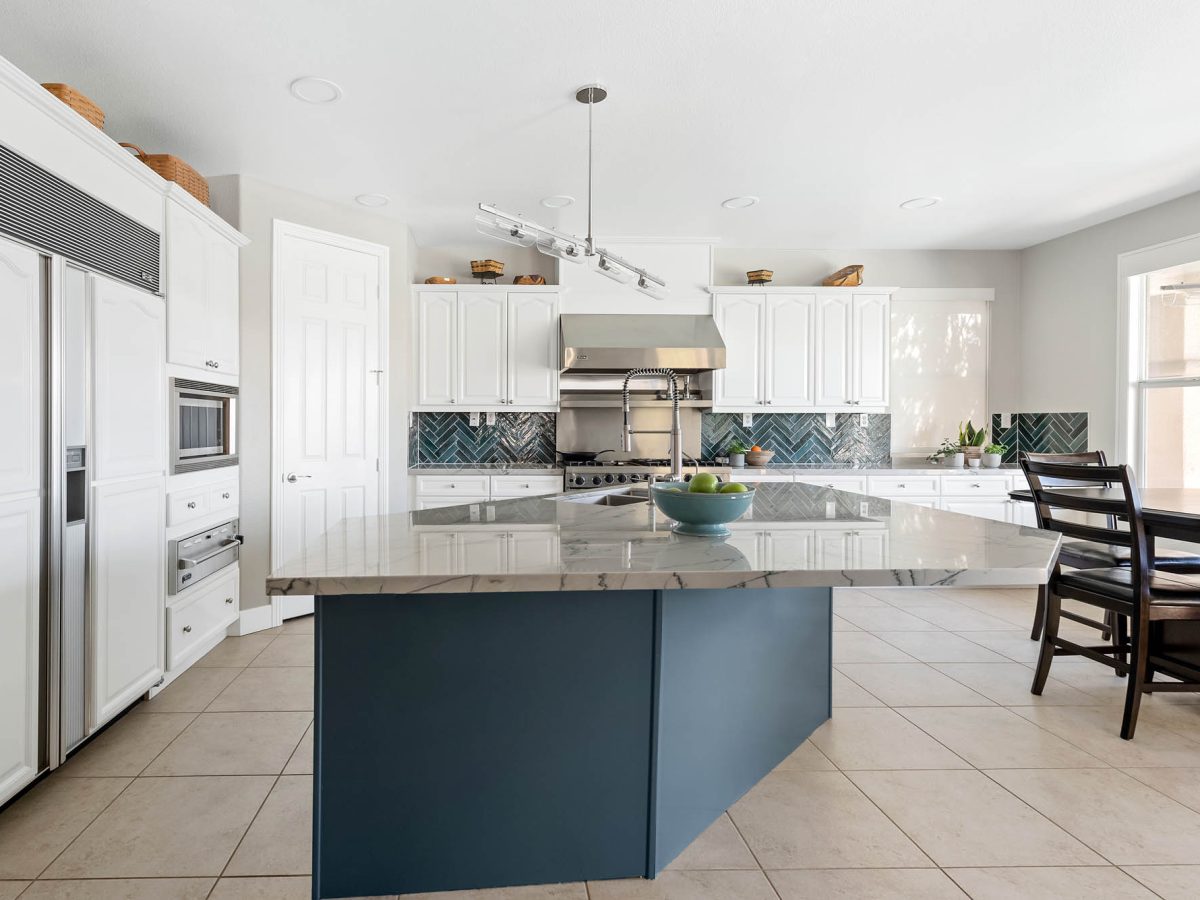 Kitchen with blue-veined quartzite island, teal herringbone backsplash, and white cabinetry, Reveal Interior Design Las Vegas