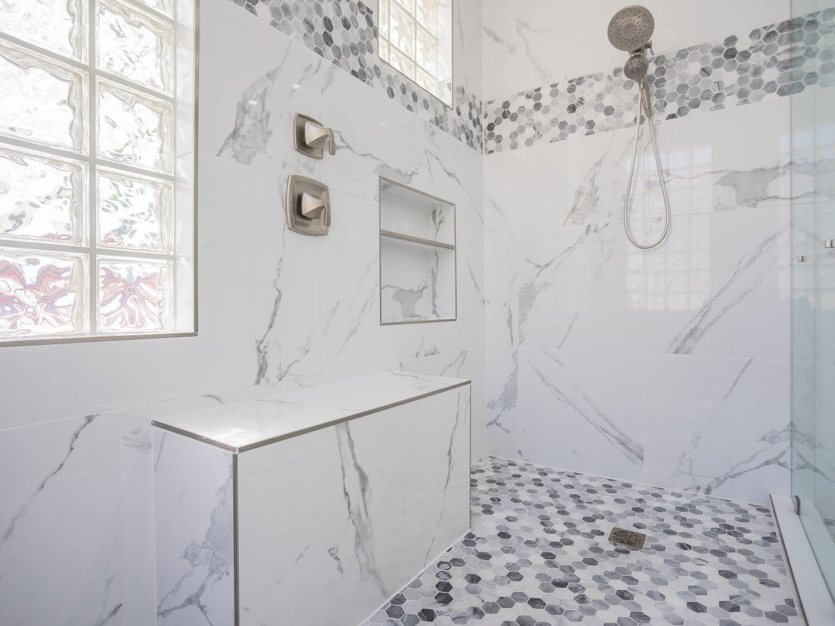 Primary bathroom with marble-look porcelain shower walls and geometric mosaic tile accents, Reveal Interior Design Las Vegas