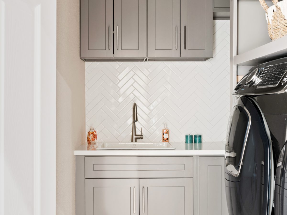 Laundry room with taupe shaker cabinets, herringbone subway tile backsplash, and encaustic floor tile, Reveal Interior Design Las Vegas
