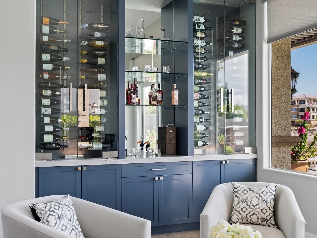 Lounge bar with blue cabinetry, glass-enclosed dual-zone wine coolers, and mirrored shelving, Reveal Interior Design Las Vegas