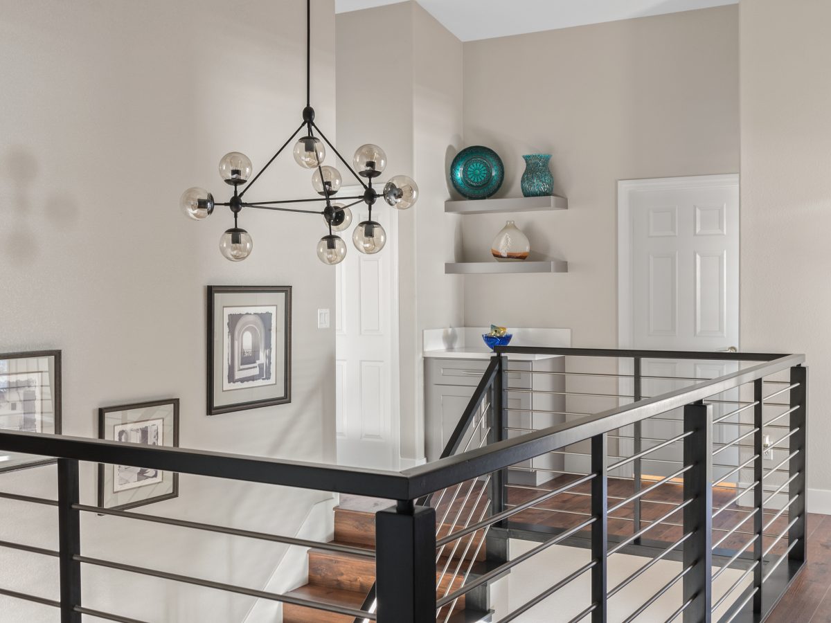 Upstairs hallway with sputnik chandelier, black metal stair railing, and floating shelves, Reveal Interior Design Las Vegas