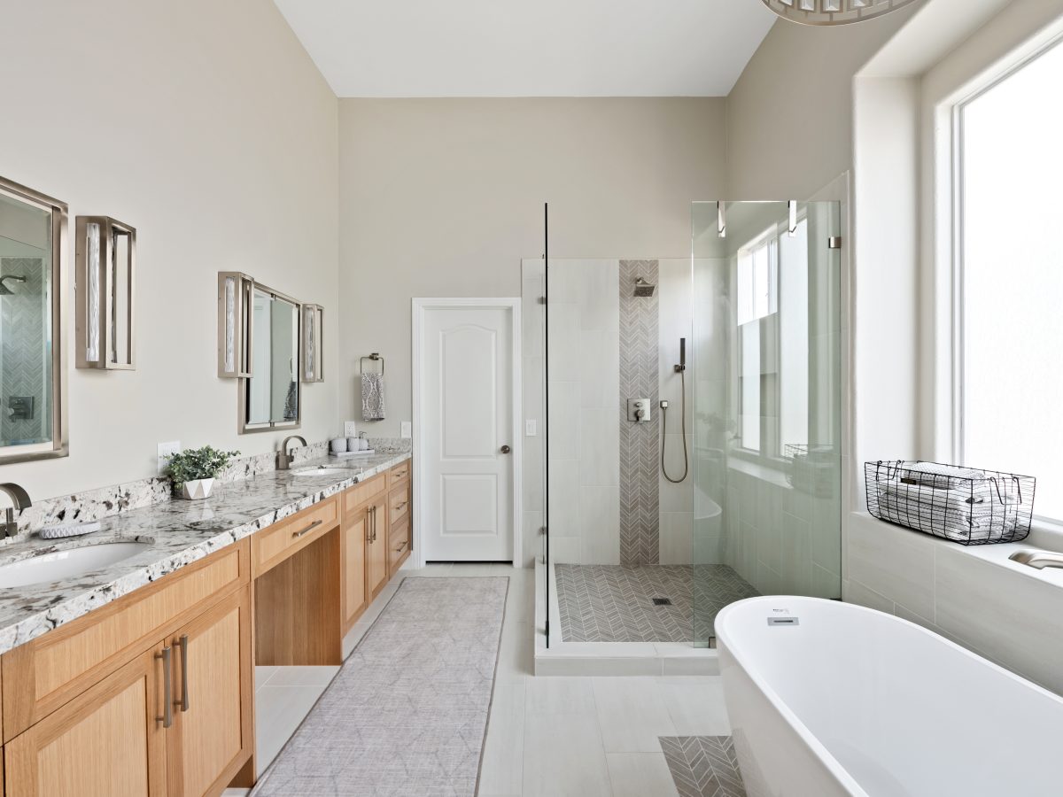 Primary bathroom with warm oak vanity, granite countertops, and glass-enclosed shower, Reveal Interior Design Las Vegas