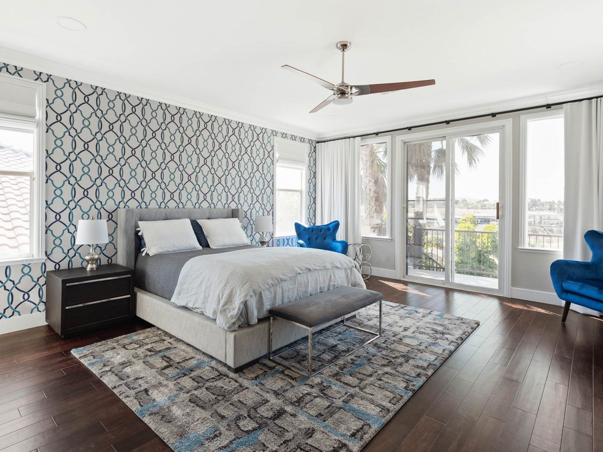 Primary bedroom with teal and navy geometric wallpaper accent wall and gray upholstered king bed, Reveal Interior Design Las Vegas