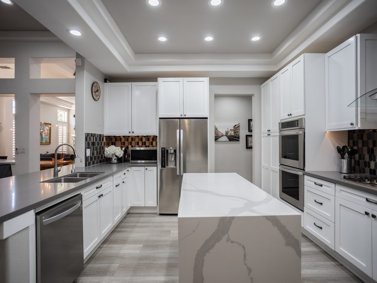 White shaker kitchen with statuario-style quartz waterfall island and hex mosaic tile backsplash, Reveal Interior Design Las Vegas