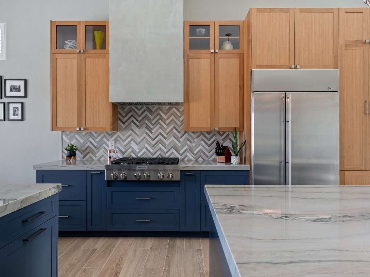 Kitchen with blue base cabinets, warm oak uppers, quartzite countertops, and herringbone mosaic backsplash, Reveal Interior Design Las Vegas