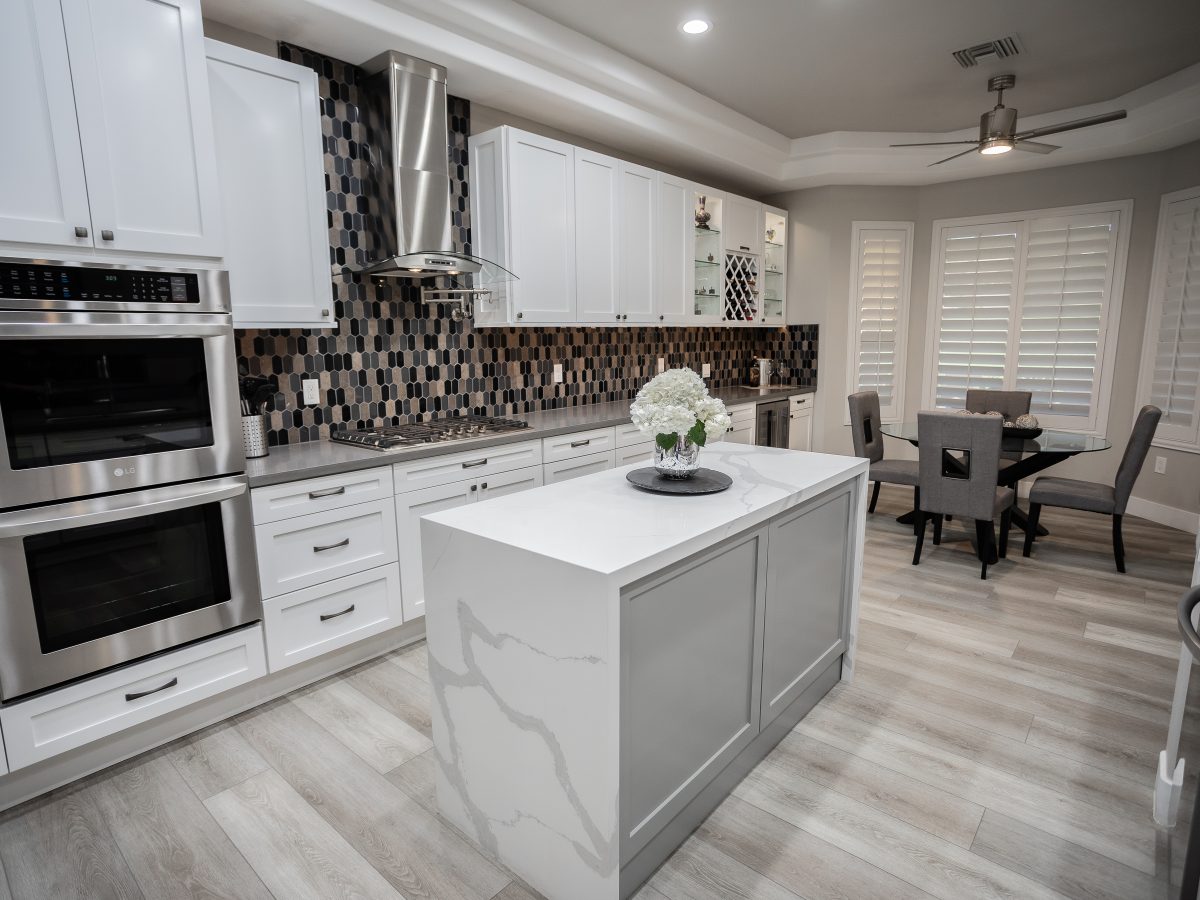 White shaker kitchen with statuario-style quartz waterfall island and hex mosaic backsplash, Reveal Interior Design Las Vegas