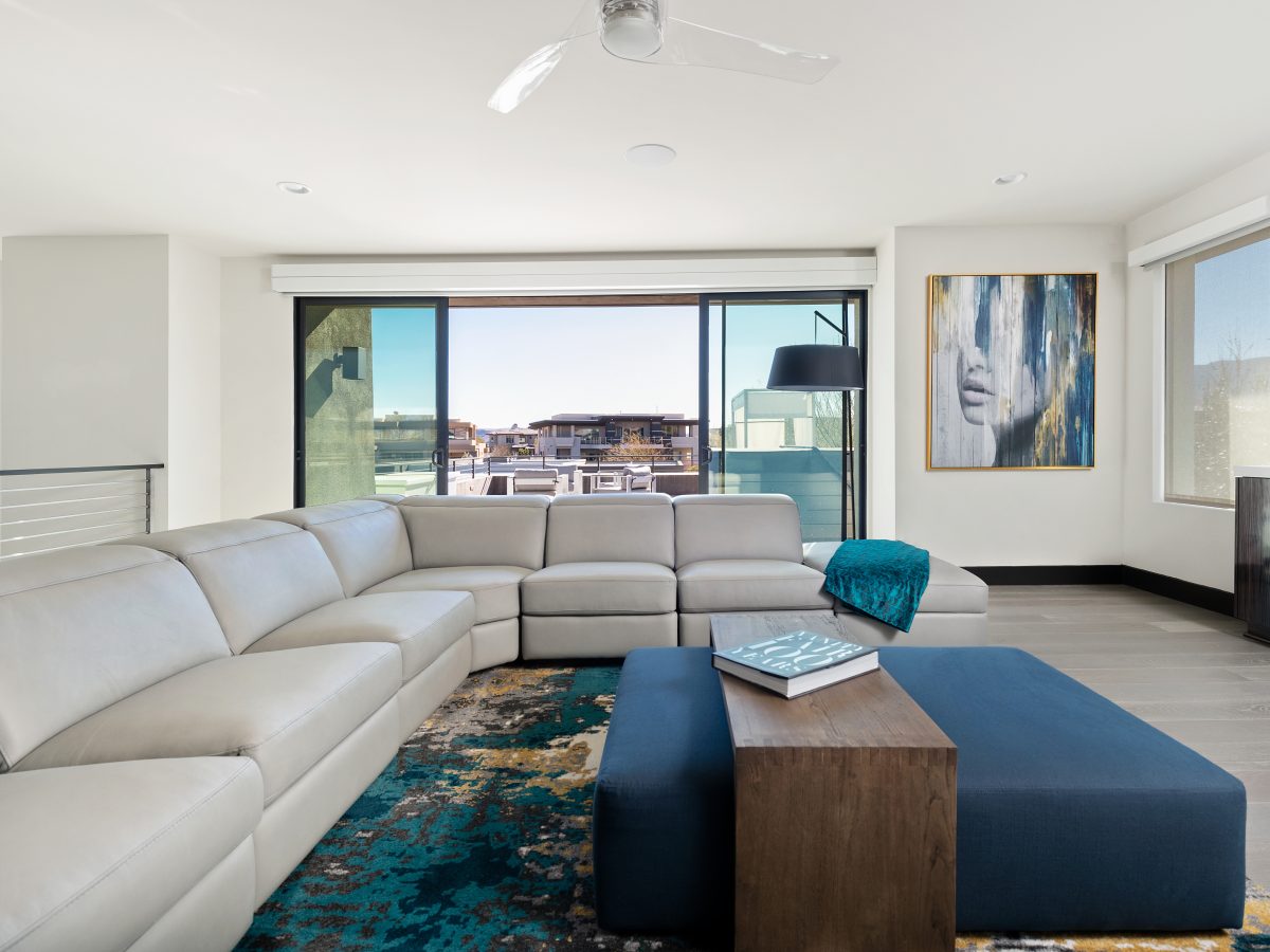 Upstairs loft seating area with leather motion sectional, deep blue ottoman, and bold teal rug, Reveal Interior Design Las Vegas