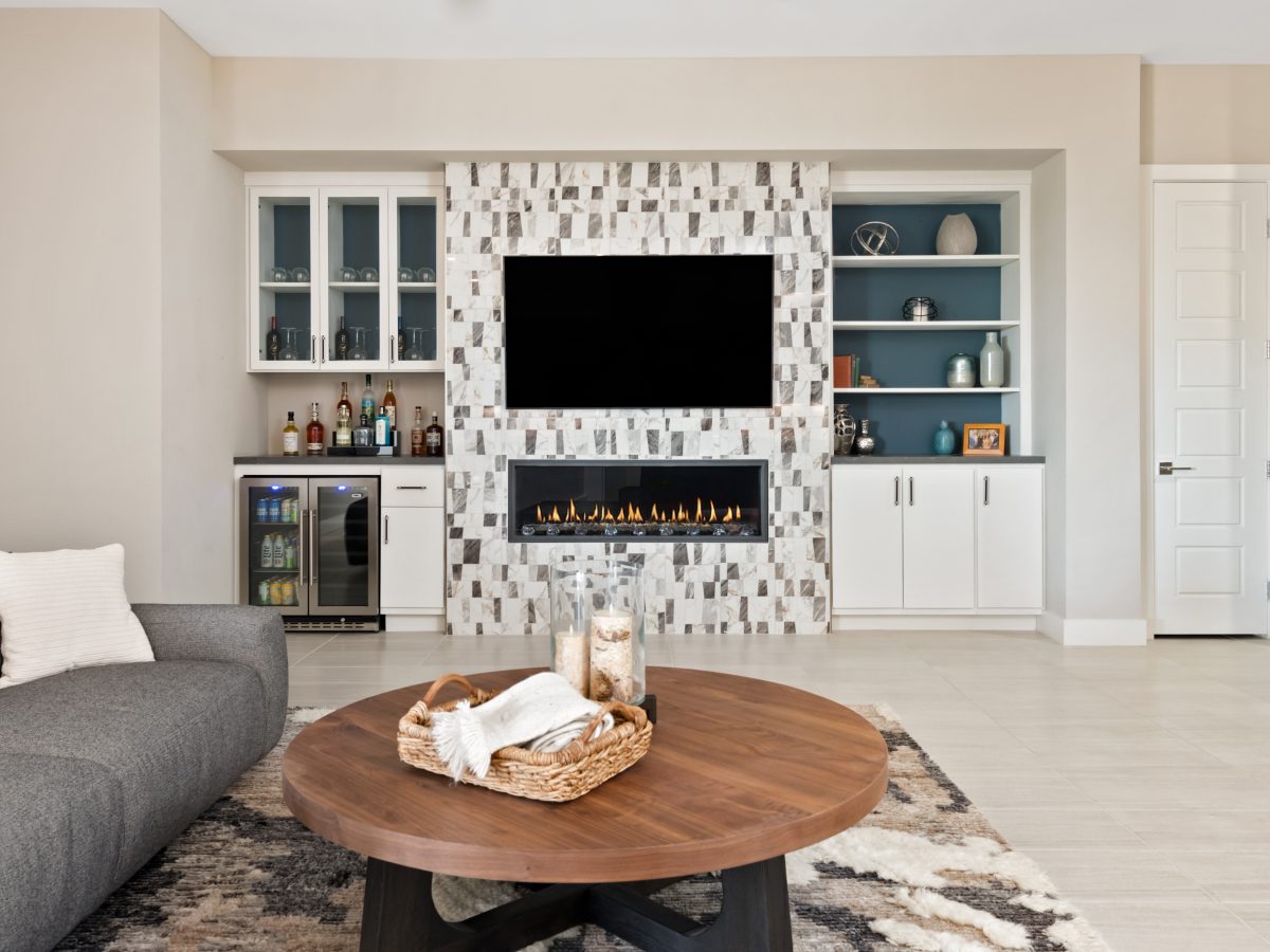Living room with linear fireplace, mosaic tile surround, built-in bar, and teal-backed custom cabinetry, Reveal Interior Design Las Vegas