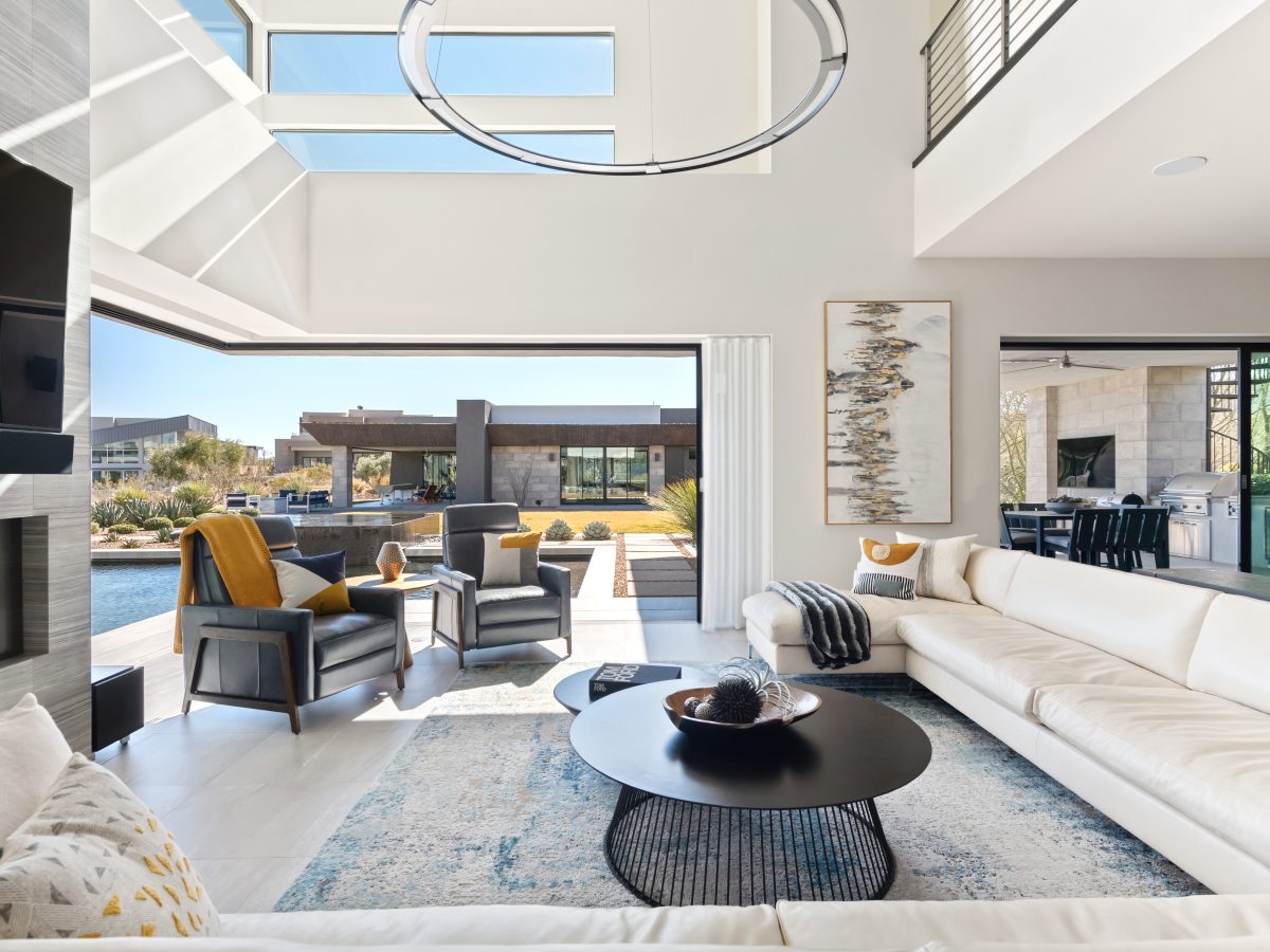 Open-concept living room with double-height ceiling, custom sectional, and indoor-outdoor slider, Reveal Interior Design Las Vegas