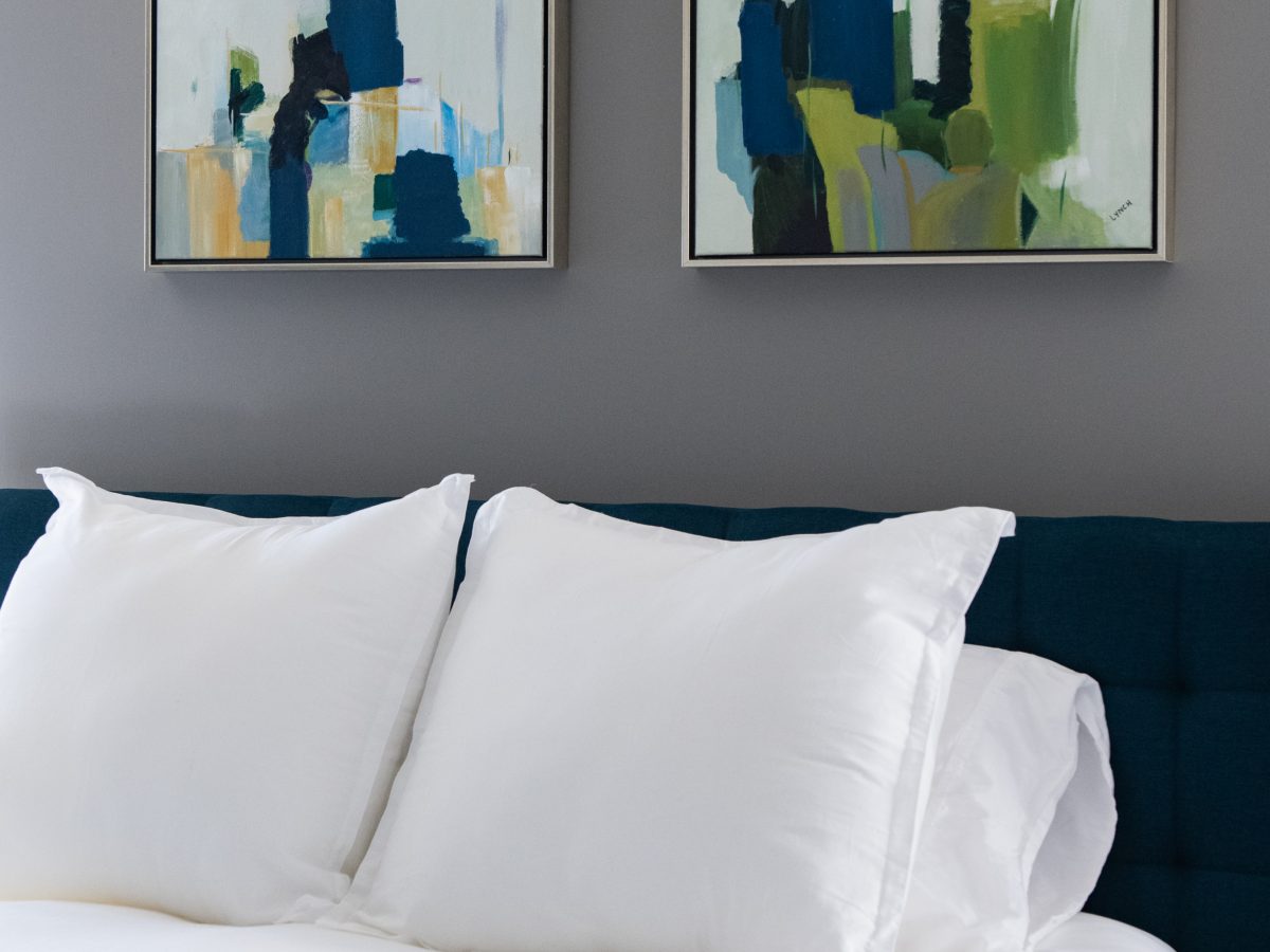 Secondary bedroom with teal upholstered headboard, abstract art diptych, and white bedding, Reveal Interior Design Las Vegas