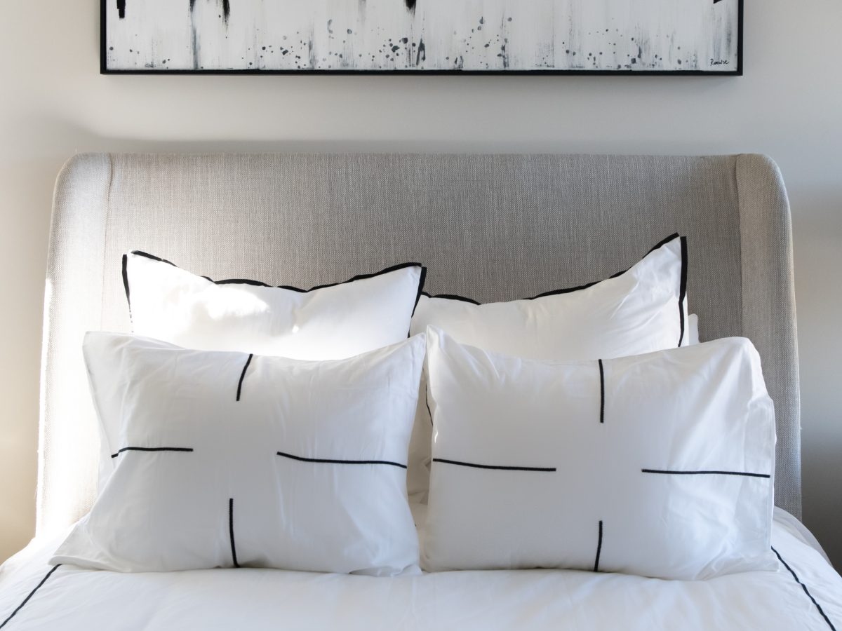 Secondary bedroom with upholstered wingback headboard, black-and-white skyline artwork, and layered white bedding, Reveal Interior Design Las Vegas
