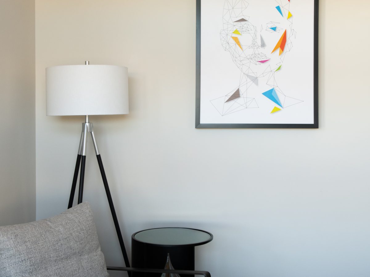 Secondary bedroom seating vignette with geometric portrait art and tripod floor lamp, Reveal Interior Design Las Vegas