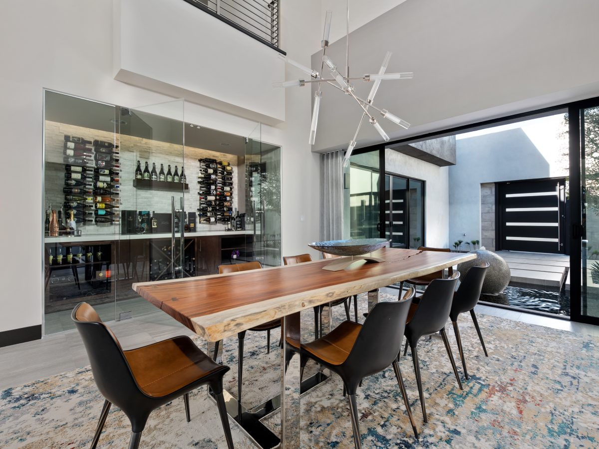 Dining room with live-edge wood table, glass-enclosed wine room, and courtyard views, Reveal Interior Design Las Vegas