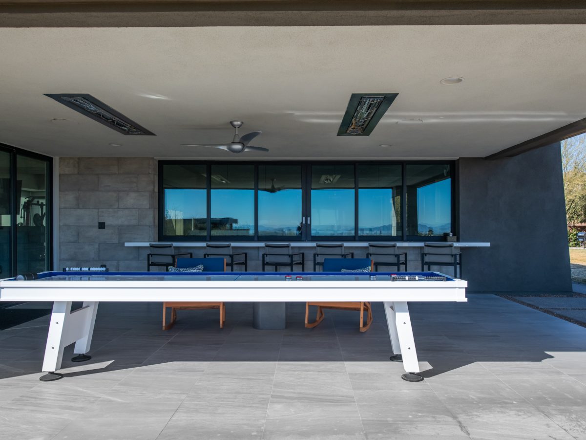Covered outdoor game and bar area with blue shuffleboard table and strip views, Reveal Interior Design Las Vegas