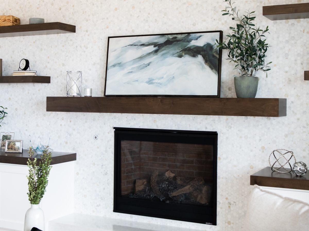 Family room fireplace wall with dark-stained wood mantel, floating shelves, and geometric marble tile, Reveal Interior Design Las Vegas