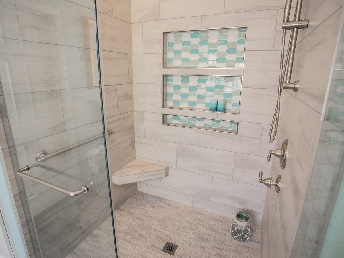 Coastal primary bathroom shower with stone-look porcelain tile, teal hex mosaic niches, and brushed nickel fixtures, Reveal Interior Design Las Vegas