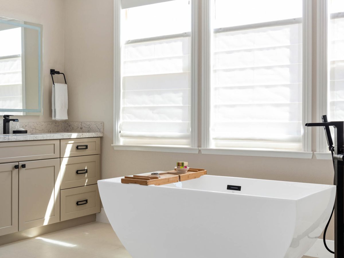 Primary bathroom with freestanding soaking tub, warm beige cabinetry, and quartz countertops, Reveal Interior Design Las Vegas