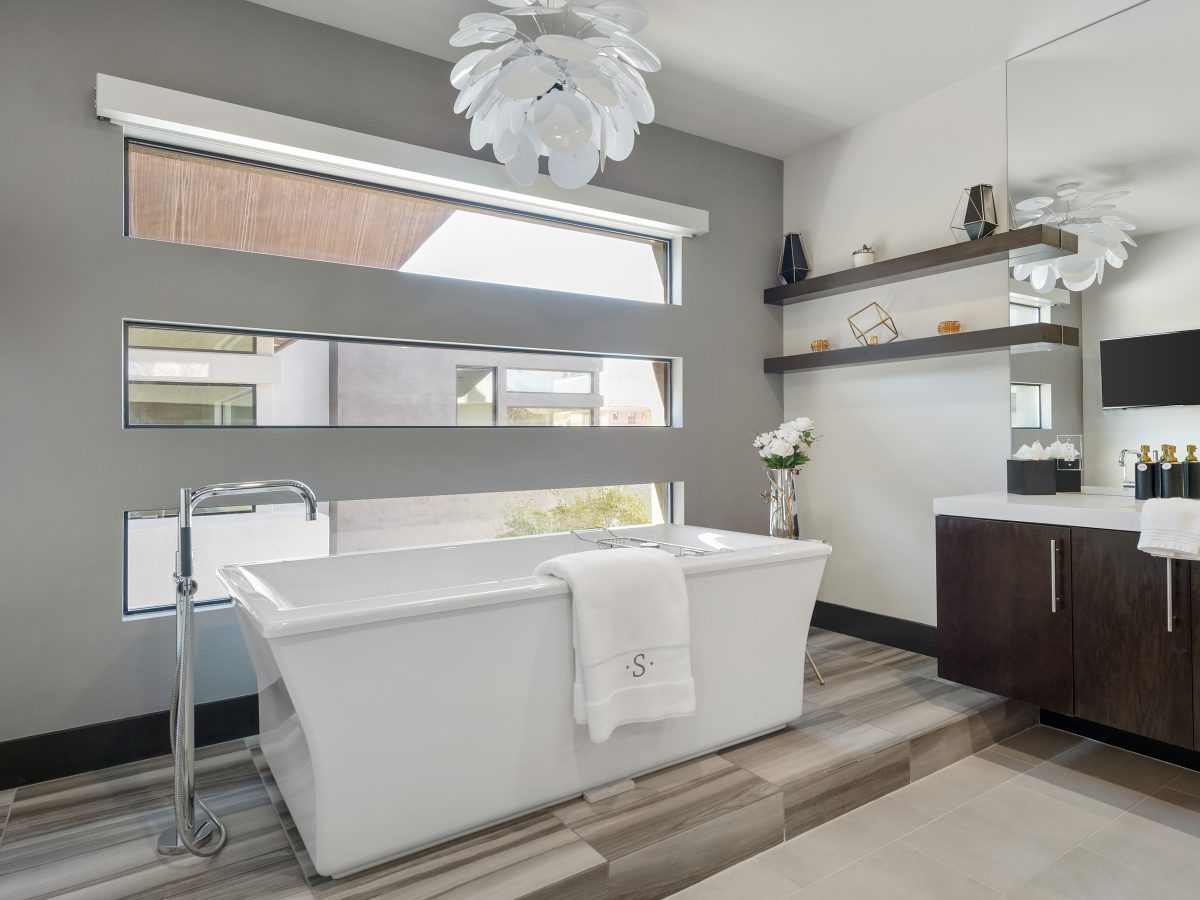 Primary bathroom with freestanding soaking tub, marble-look porcelain slab, and petal chandelier, Reveal Interior Design Las Vegas