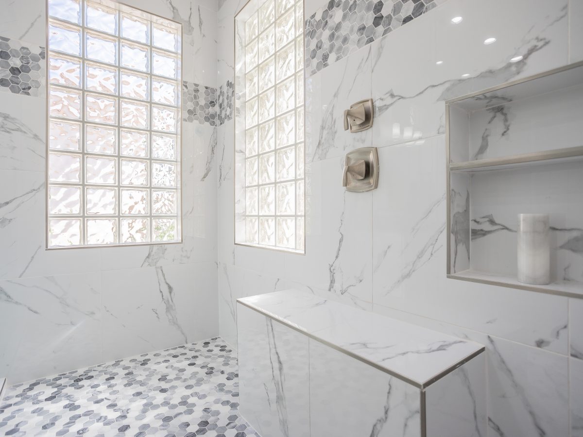 Expansive primary bathroom shower with marble-look porcelain tile walls and geometric mosaic accents, Reveal Interior Design Las Vegas