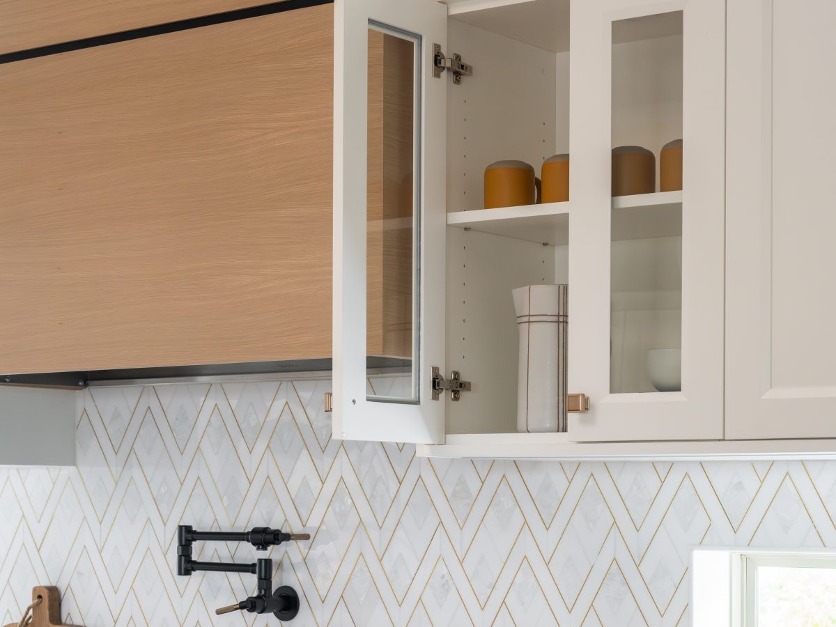Kitchen with custom wood hood, geometric stone backsplash, and glass-front upper cabinets, Reveal Interior Design Las Vegas