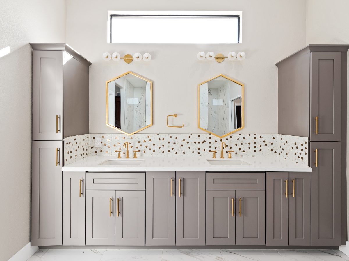 Primary bathroom double vanity with taupe shaker cabinets, gold fixtures, and geometric mirrors, Reveal Interior Design Las Vegas