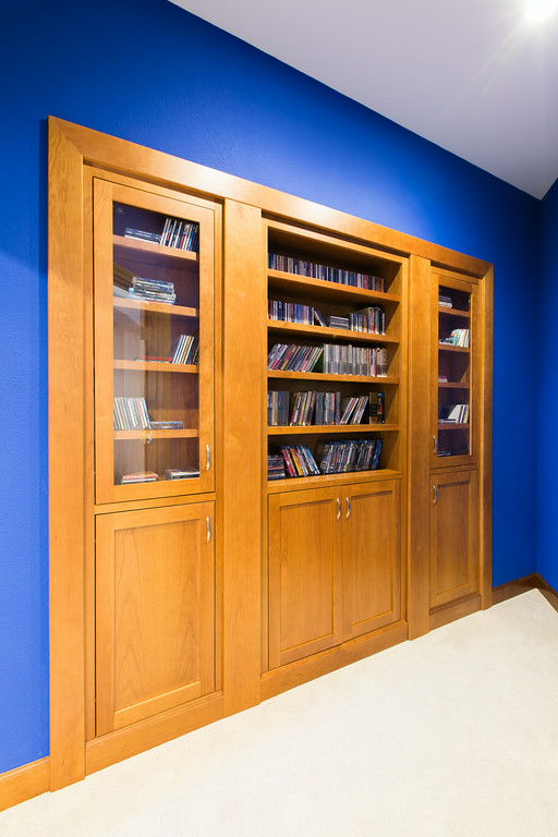 Home theater with deep blue walls, maple millwork accents, and hidden bookcase door, Reveal Interior Design Las Vegas