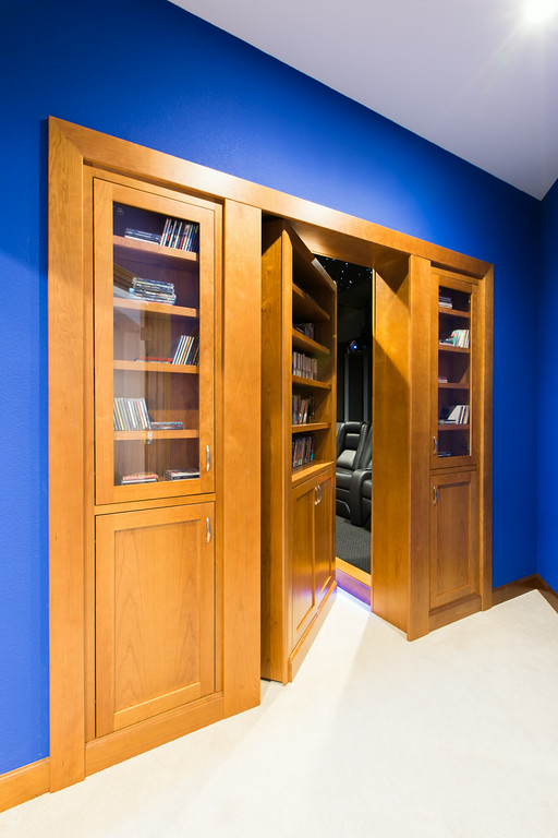 Home theater with hidden maple bookcase door, cobalt blue walls, and raised seating platform, Reveal Interior Design Las Vegas