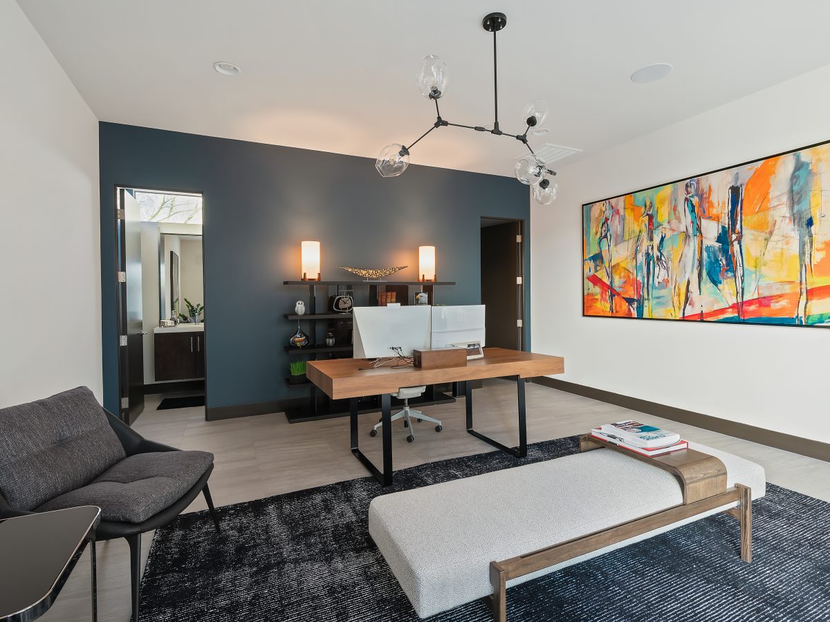 Home office with slate blue accent wall, wood desk, and oversized abstract artwork, Reveal Interior Design Las Vegas