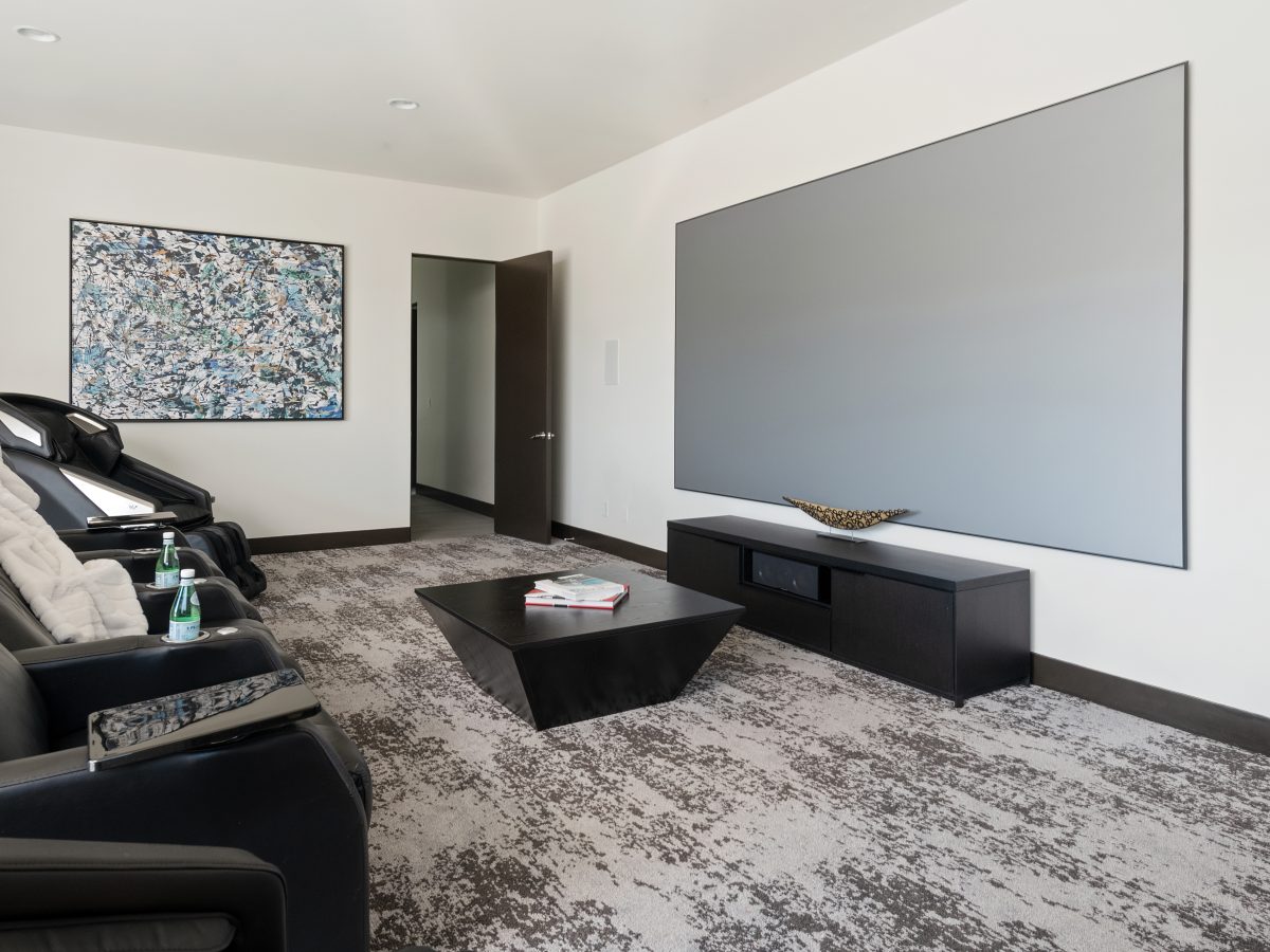 Home theater with leather recliners, geometric black coffee table, and expansive movie screen, Reveal Interior Design Las Vegas