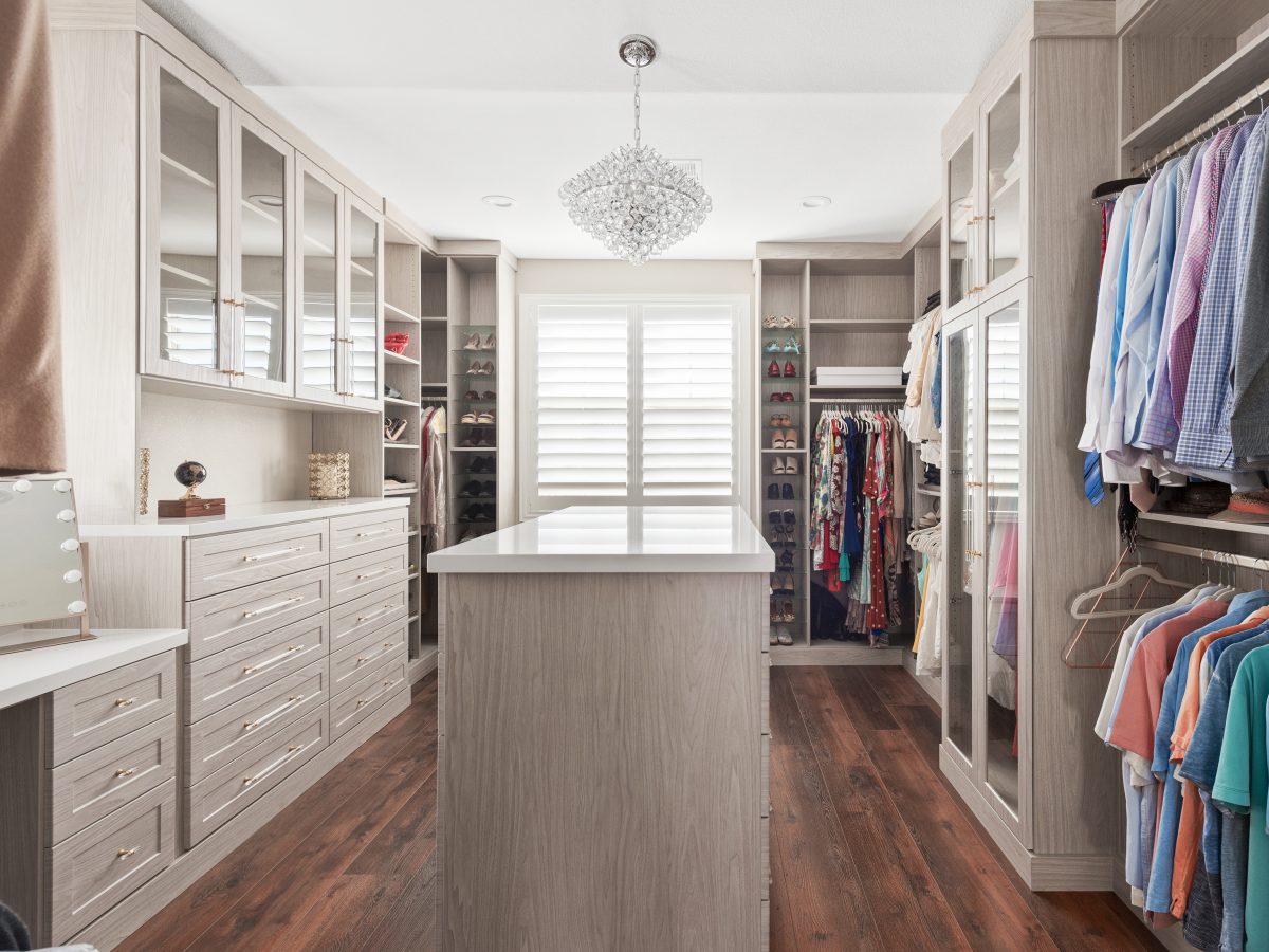 Large walk-in closet with taupe cabinetry, quartz island, and crystal chandelier, Reveal Interior Design Las Vegas