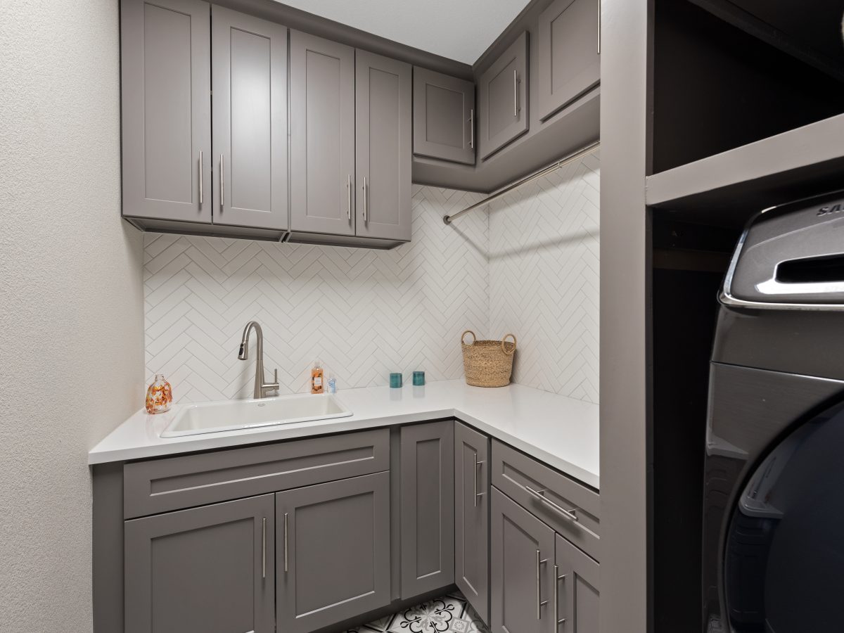 Laundry room with taupe shaker cabinetry, white quartz counters, and herringbone subway tile, Reveal Interior Design Las Vegas
