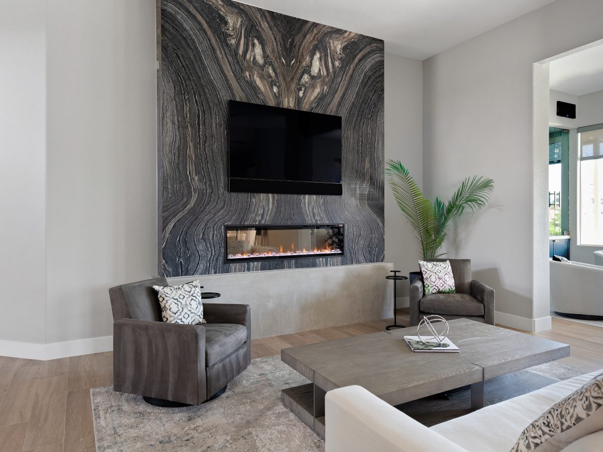 Living room with bookmatched leathered quartzite feature wall, linear fireplace, and modern swivel seating, Reveal Interior Design Las Vegas